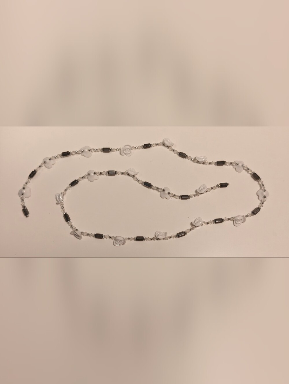 Long statement necklace features magnetic hematite and white rose flower beads